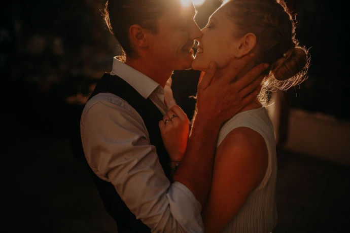 Gros plan d'un couple de mariés s'embrassant tendrement à contre-jour lors d'une réception en extérieur au coucher du soleil.