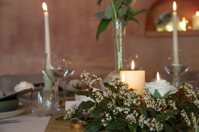 Décoration de table de mariage chaleureuse avec bougies allumées, compositions florales délicates et verres à vin sur nappe blanche.