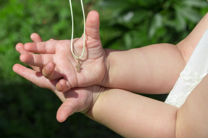 Gros plan sur les mains d'un enfant tenant un petit pendentif en forme de croix dorée lors d'un baptême chrétien.