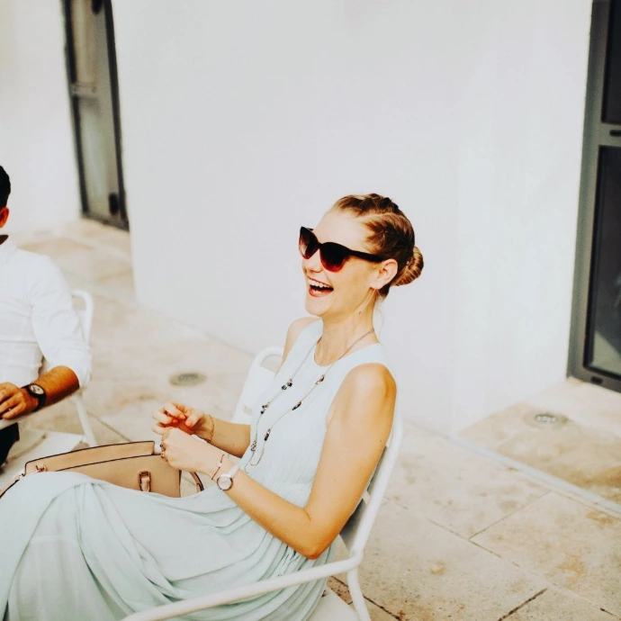 Portrait spontané d'une jeune femme riant aux éclats, portant des lunettes de soleil rouges lors d'un cocktail de mariage en extérieur.